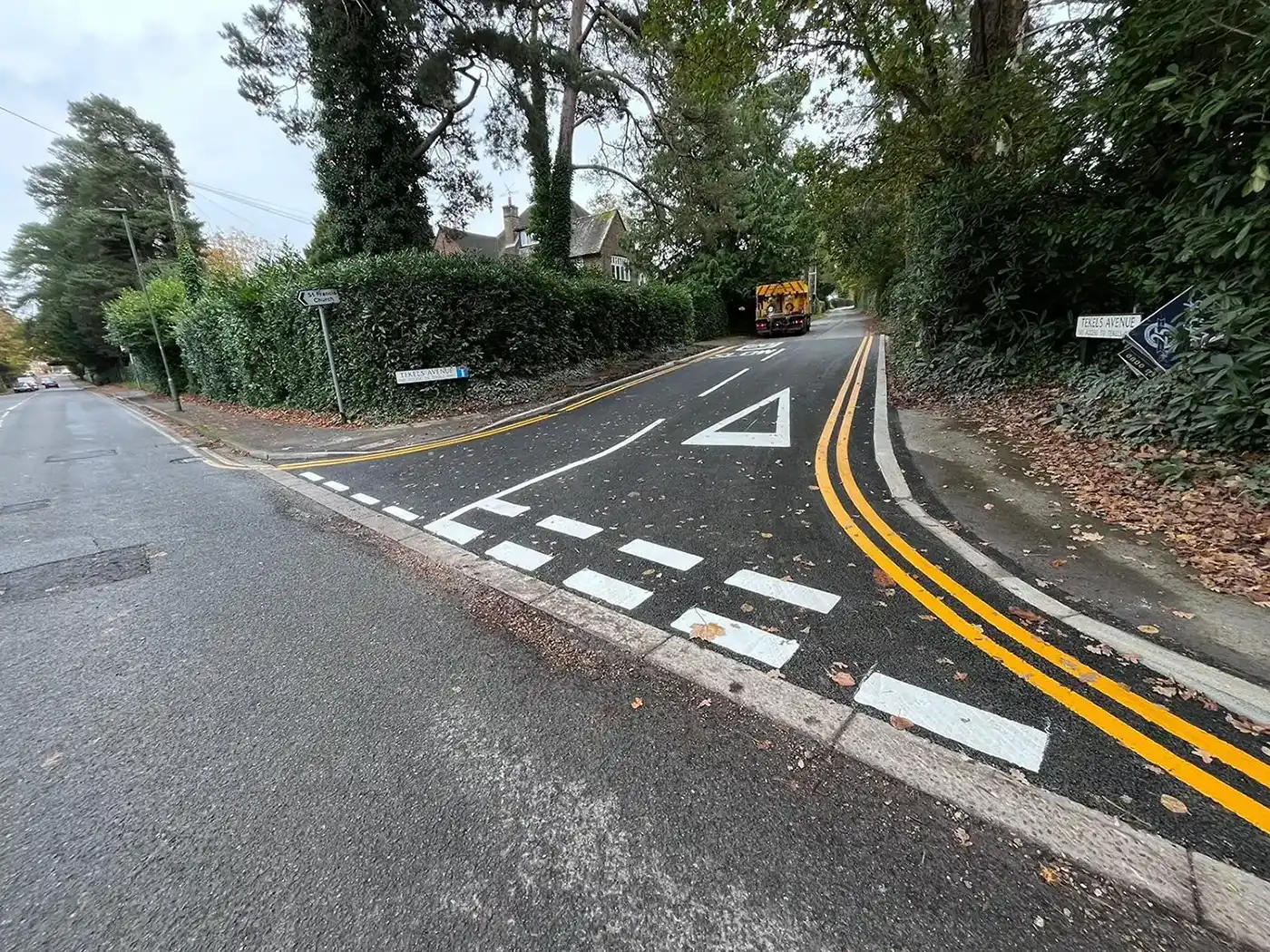 A road intersection with a curved path, directional signs, and a vehicle approaching. Surrounding green foliage is visible.